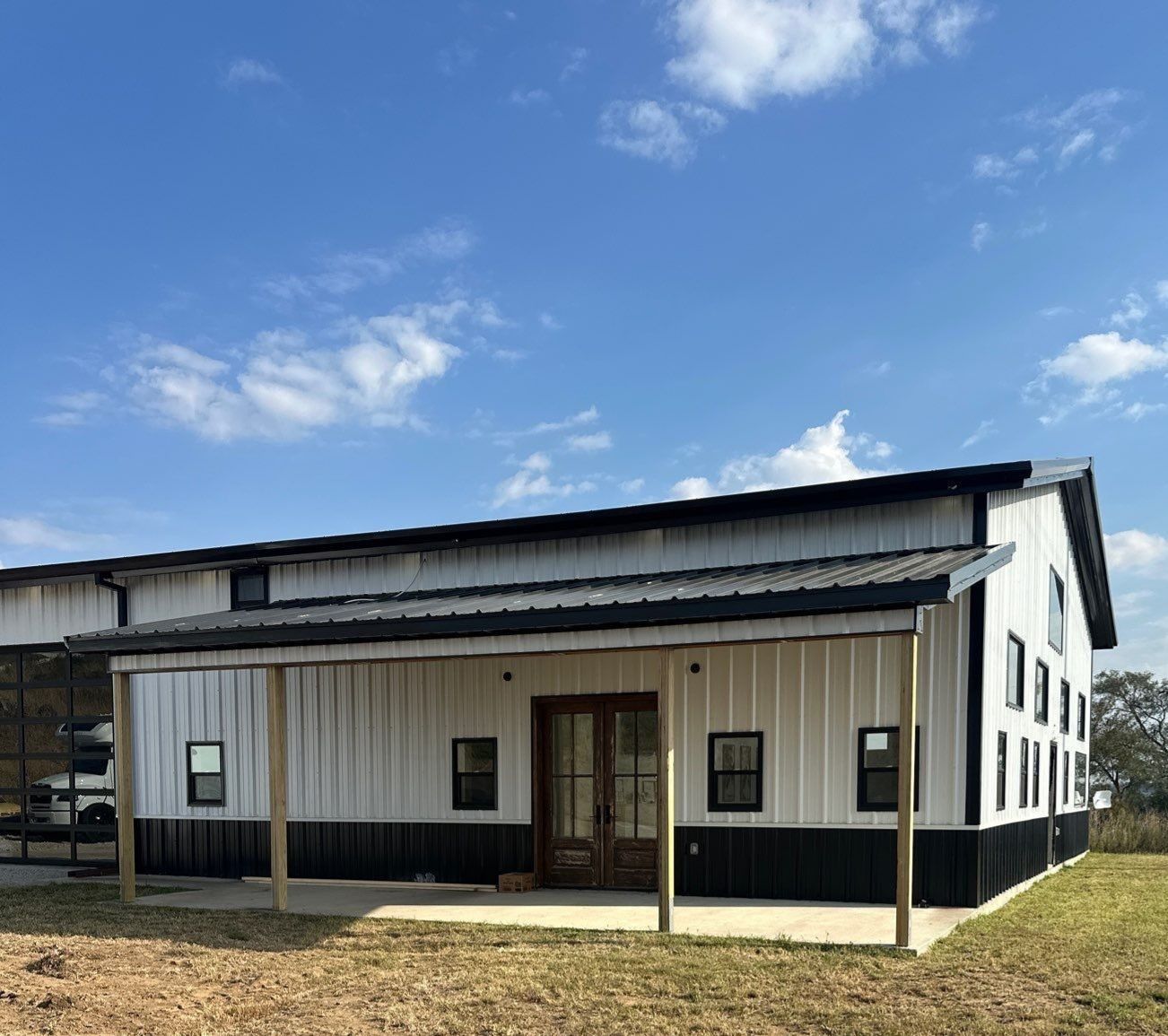 White and black barn-style building with a porch and black roof against a blue sky.