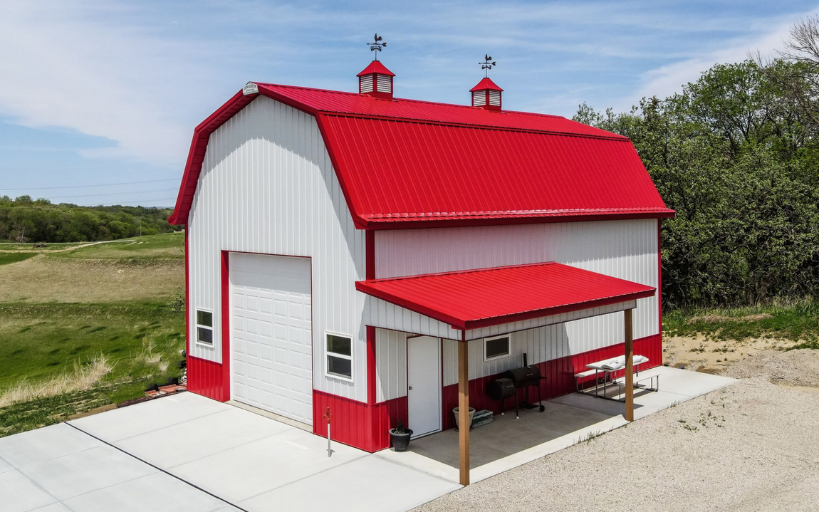 Red barn with white trim and sliding doors, gravel path, and blue sky.