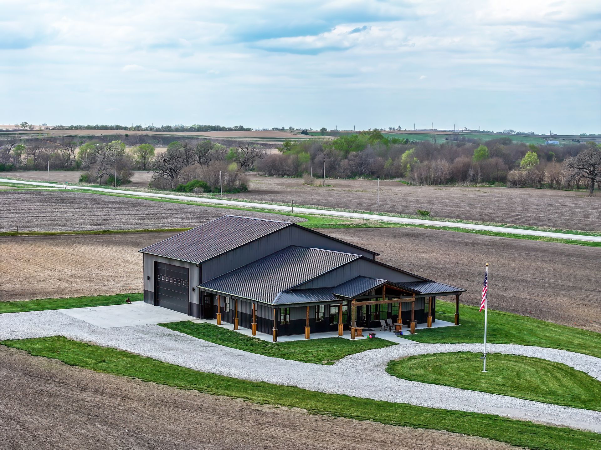Modern black home with garage and porch on rural property, gravel driveway, American flag.