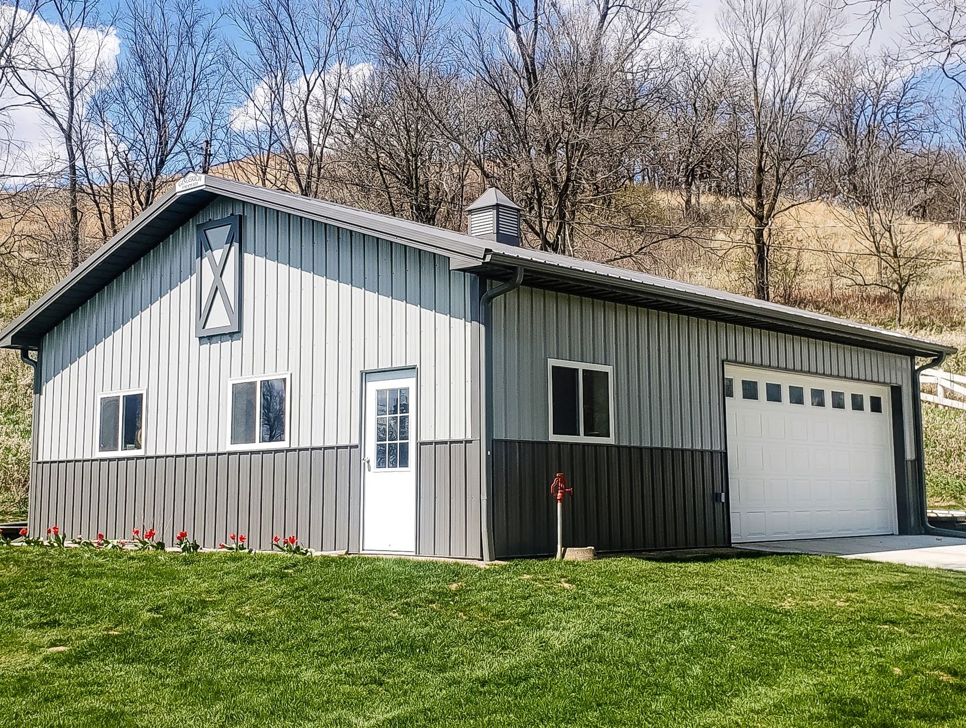 Gray and dark gray metal-sided building with white garage door, windows, and door on green lawn.