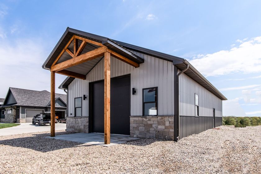 A light gray and black metal building with a stone base, a brown wooden porch, and a black roof.