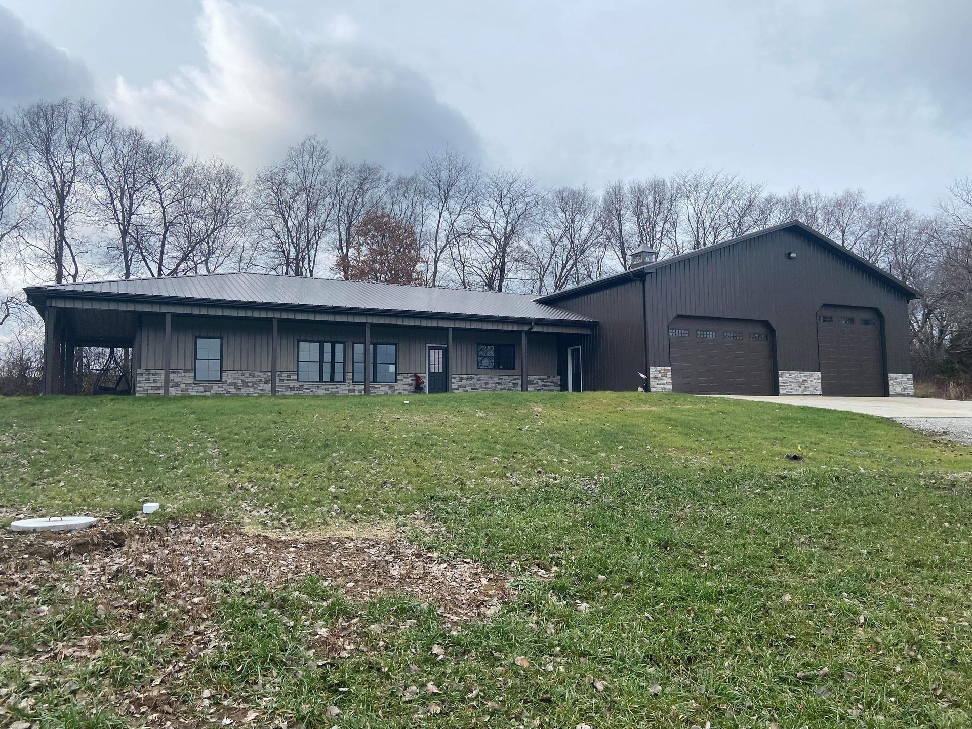 Brown house with attached garage, stone accents, and green lawn under a cloudy sky.