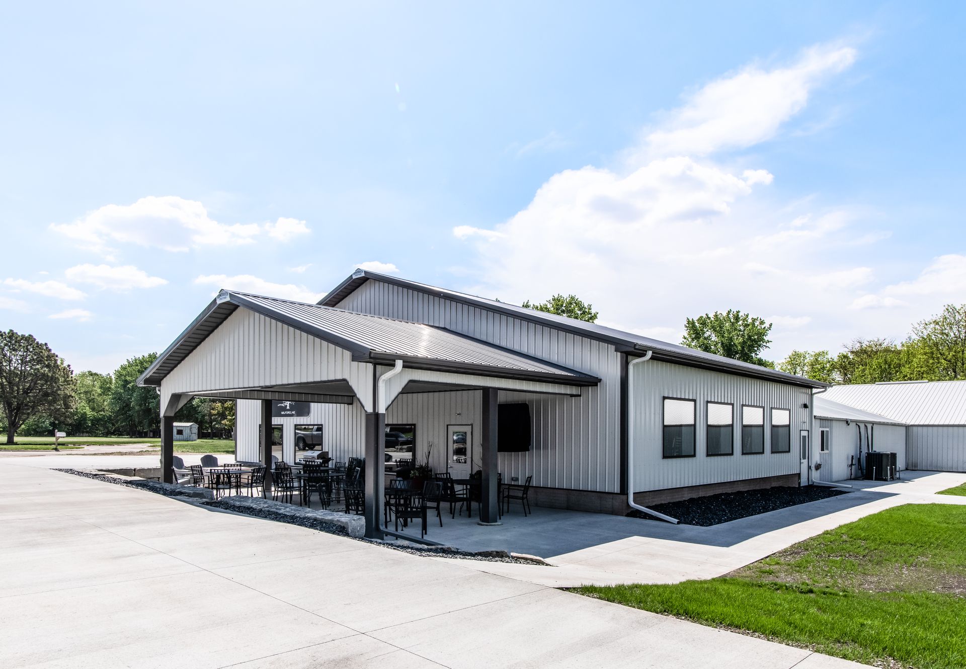 White, barn-like building with a covered outdoor seating area on a sunny day.