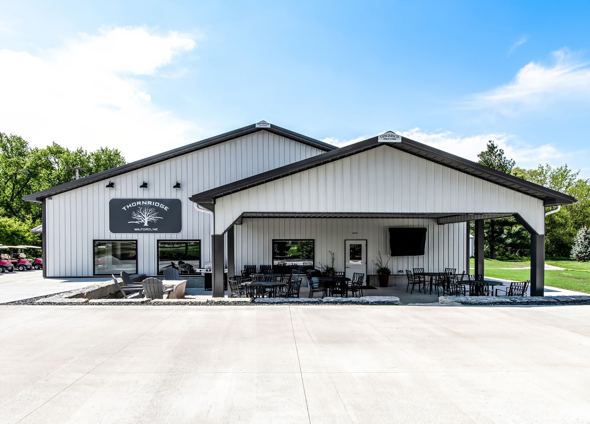 White building with a covered patio, tables, and chairs. Logo on the side. Bright, sunny day.