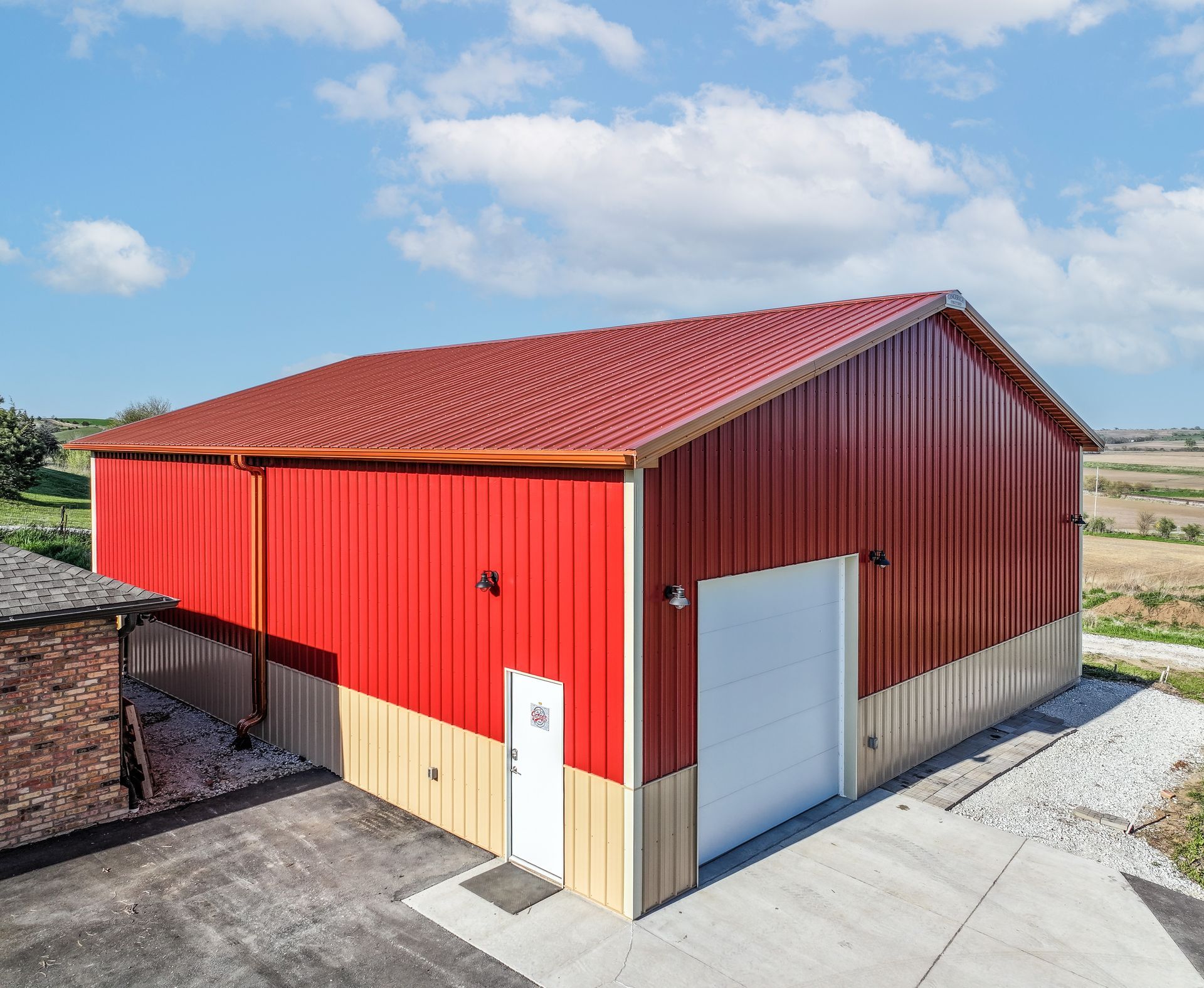 Red and tan metal building with a red roof and white garage door, under a blue sky.