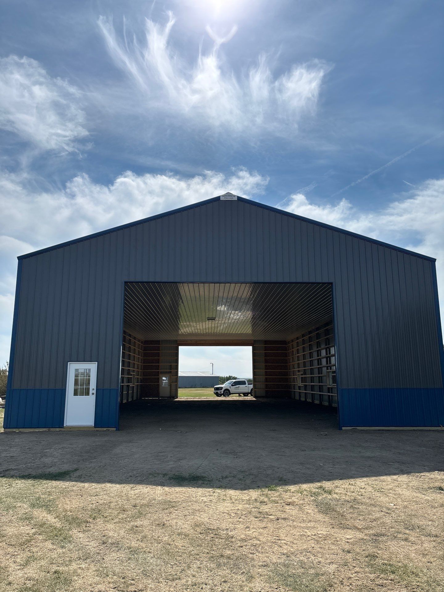 Metal building with open front and white door, blue trim, and blue sky.