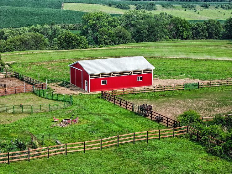 Red barn on a green farm, with wooden fences and crops. Rolling hills in the background.