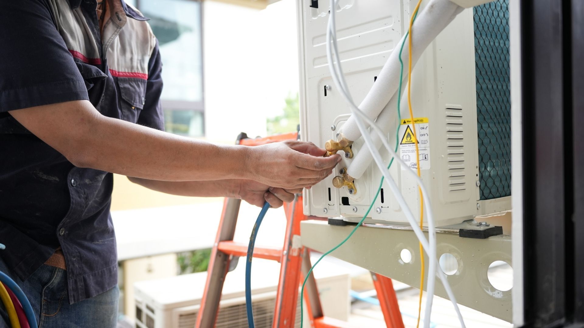 HVAC technician repairs an outdoor unit, connecting tubes with hands. Light blue tubes.
