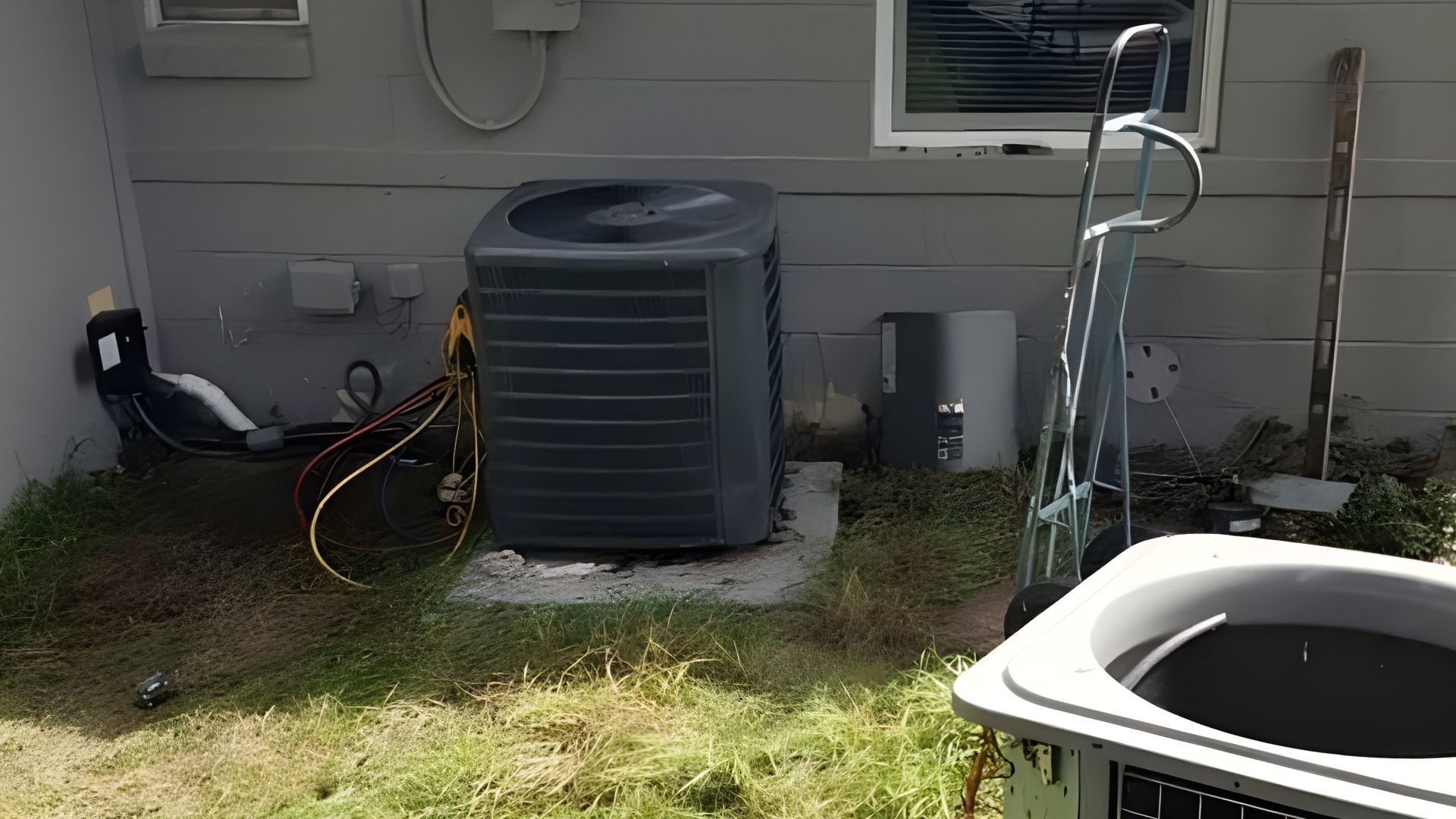 HVAC unit on a concrete pad next to a house with tools and equipment in the yard.
