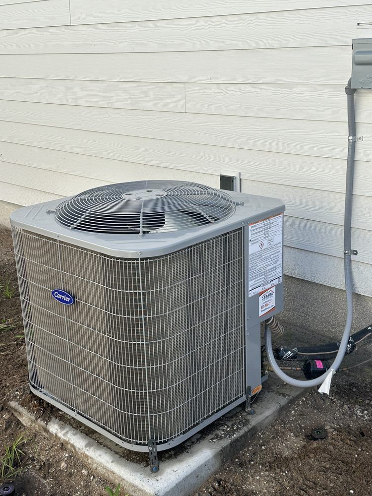 Gray Carrier air conditioning unit next to a white house with a grey electrical conduit.