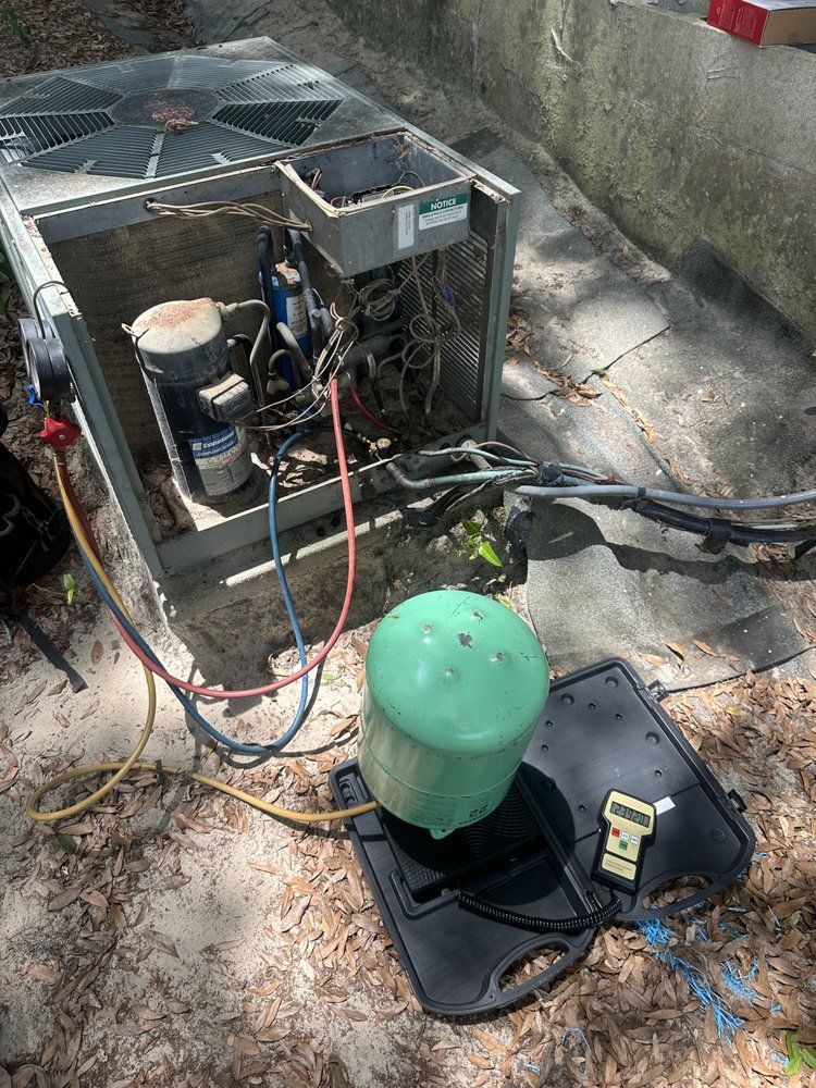 HVAC unit with hoses connected to a green refrigerant tank on a black tool case outdoors.