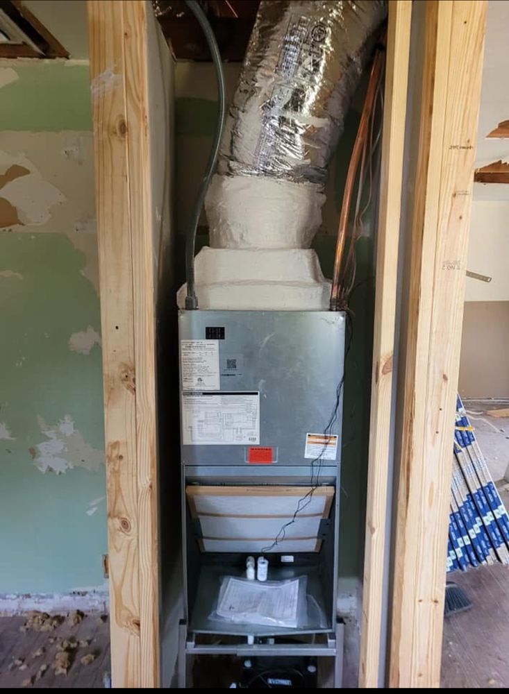Furnace unit installed between wooden studs in a room under renovation.