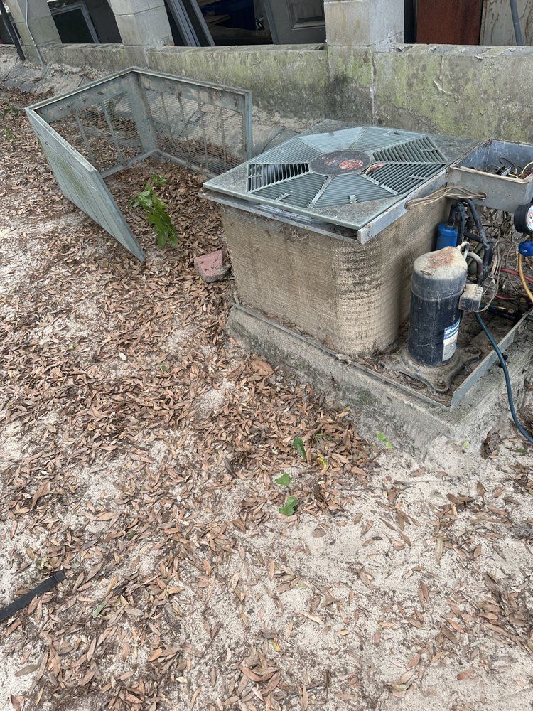 Outdoor air conditioning unit with broken metal cage and surrounding leaves.