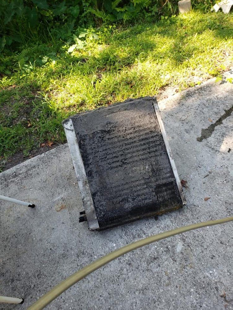 Dirty, rectangular air conditioning unit on a concrete surface with a garden hose nearby.