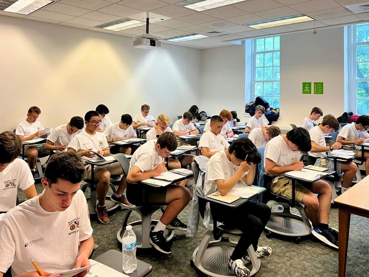 A group of young men are sitting at desks in a classroom taking an exam