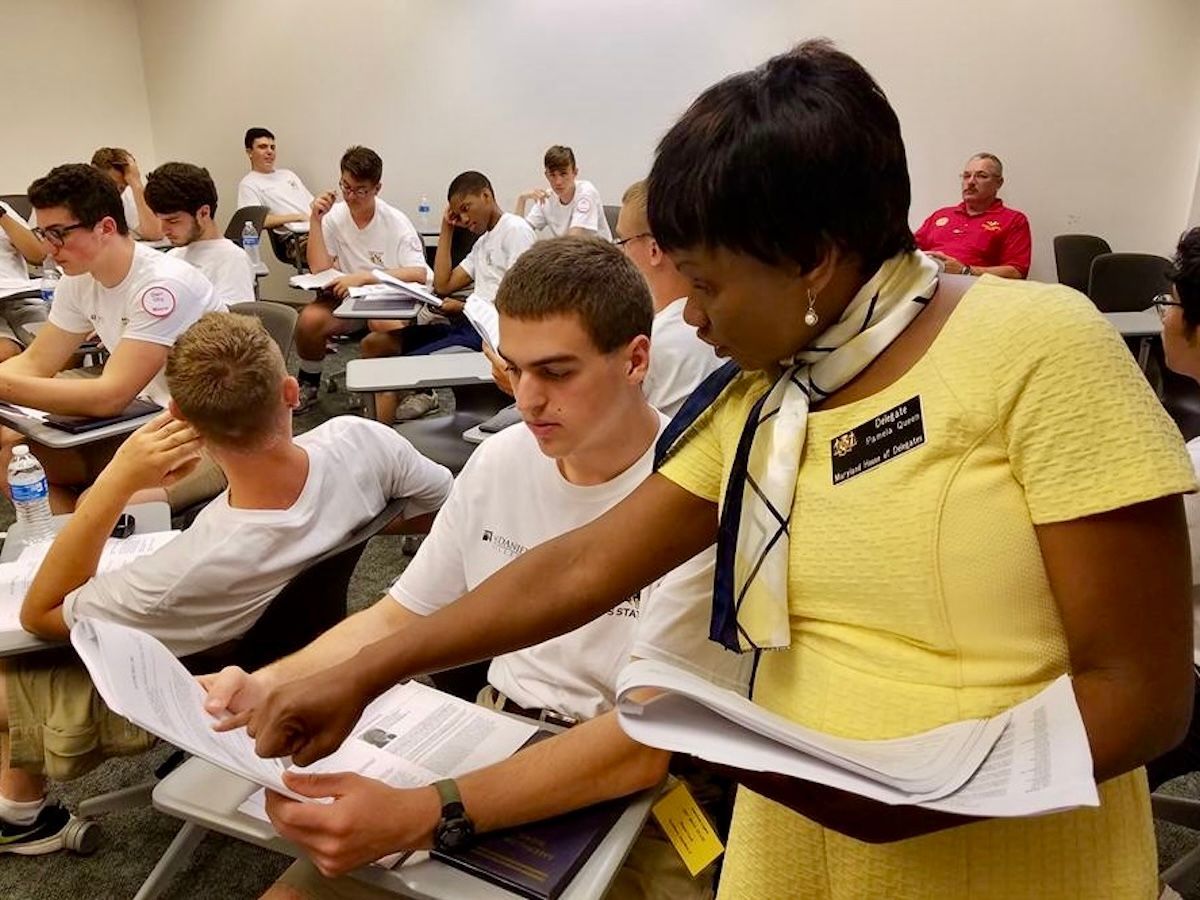A woman in a yellow dress is talking to a group of students in a classroom