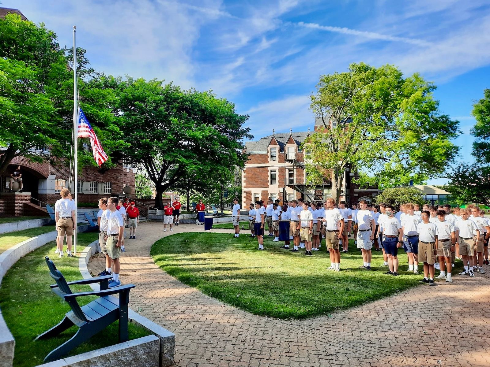 A group of young men standing at attention in front of a flag in a park on a sunny evening