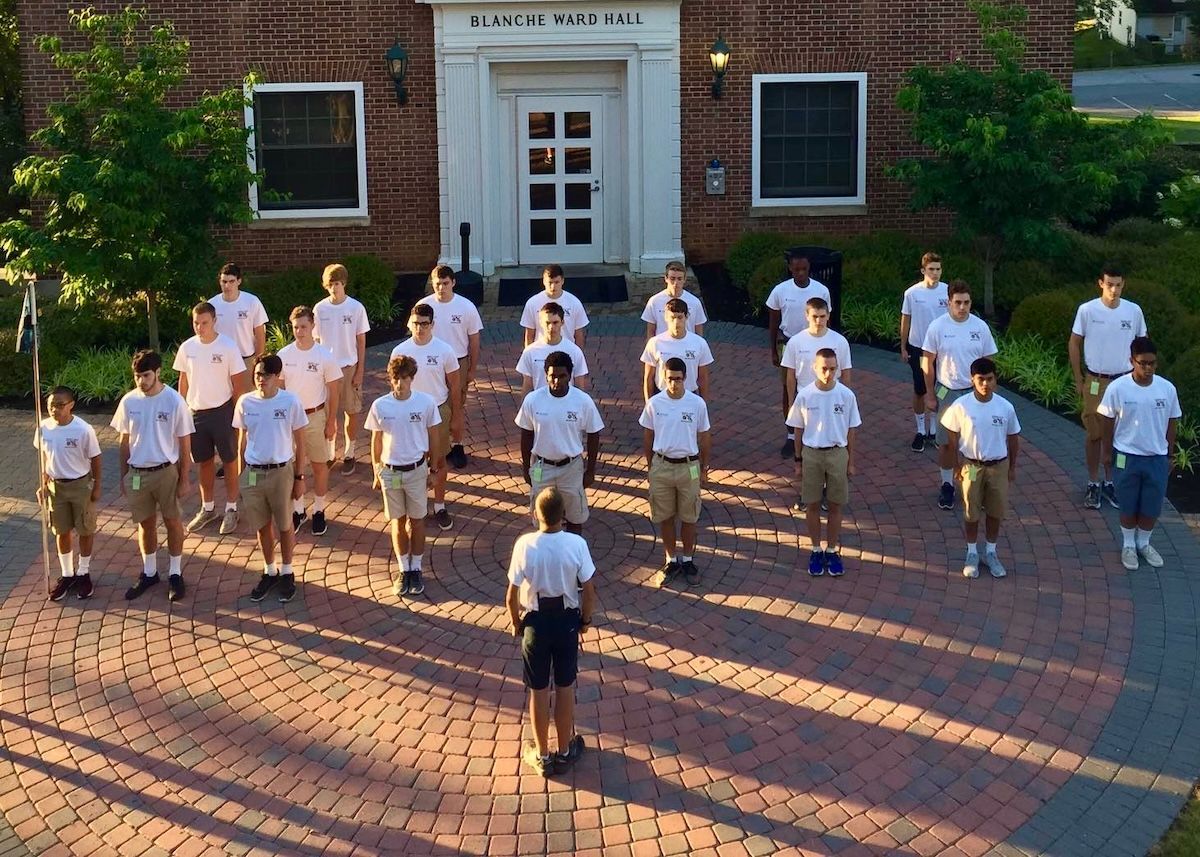 A group of boys are standing in formation in front of a brick building