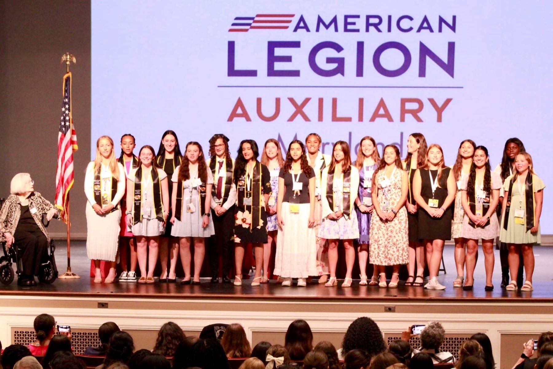A group of young women are standing on a stage in front of an American Legion Auxiliary logo