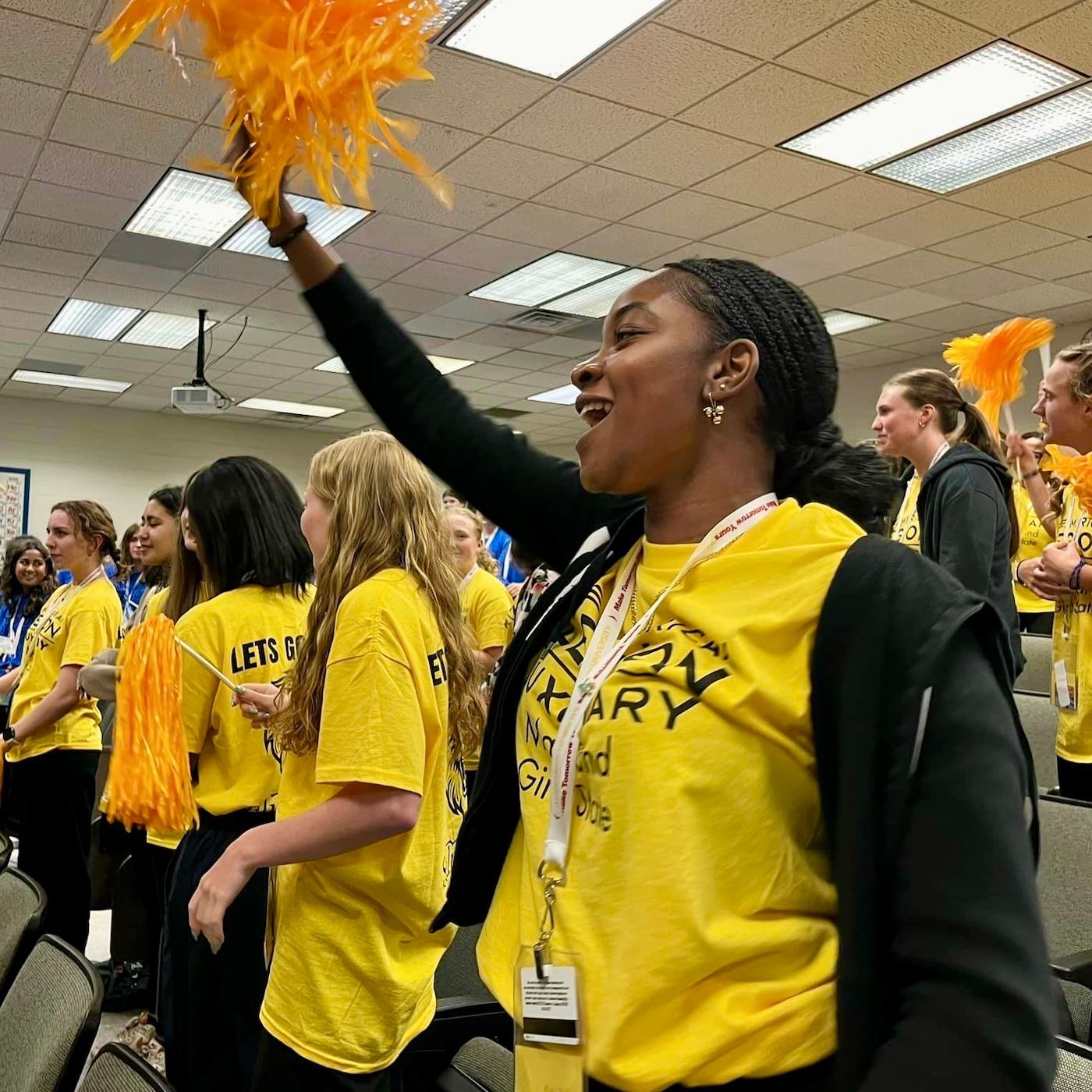 A group of young women wearing yellow shirts are cheering in an auditorium
