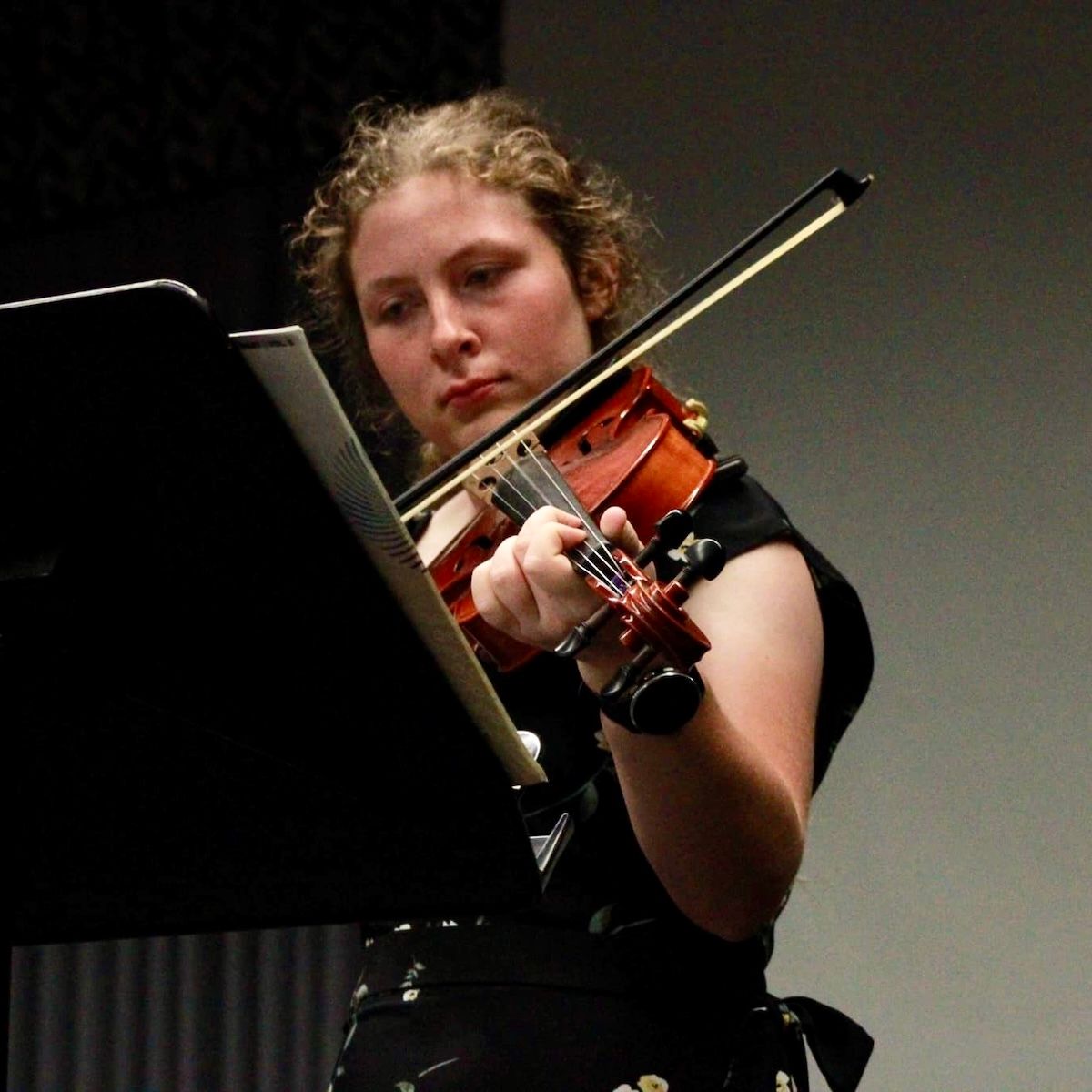 A young woman in a black dress is playing a violin
