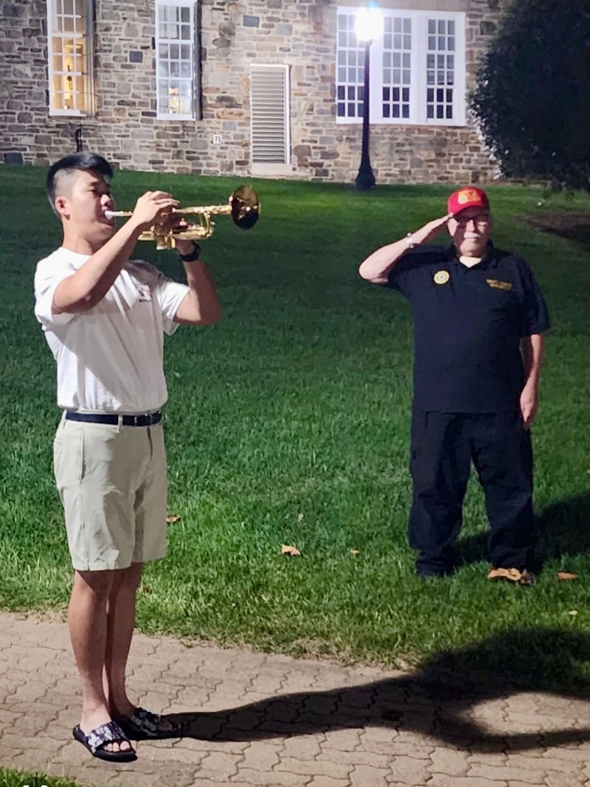 A young man is playing a trumpet while another man salutes