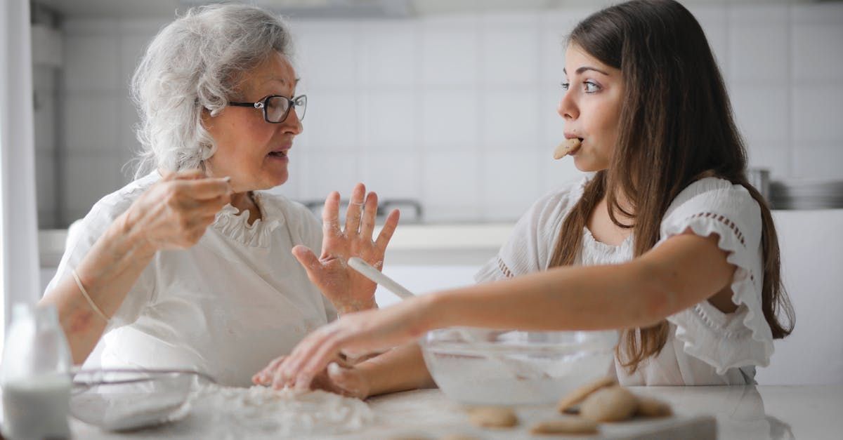 An elderly woman and a young girl are sitting at a table eating cookies.