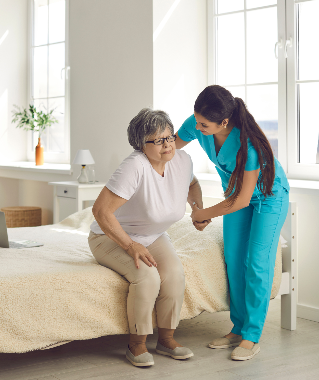 A nurse is helping an elderly woman sit on a bed
