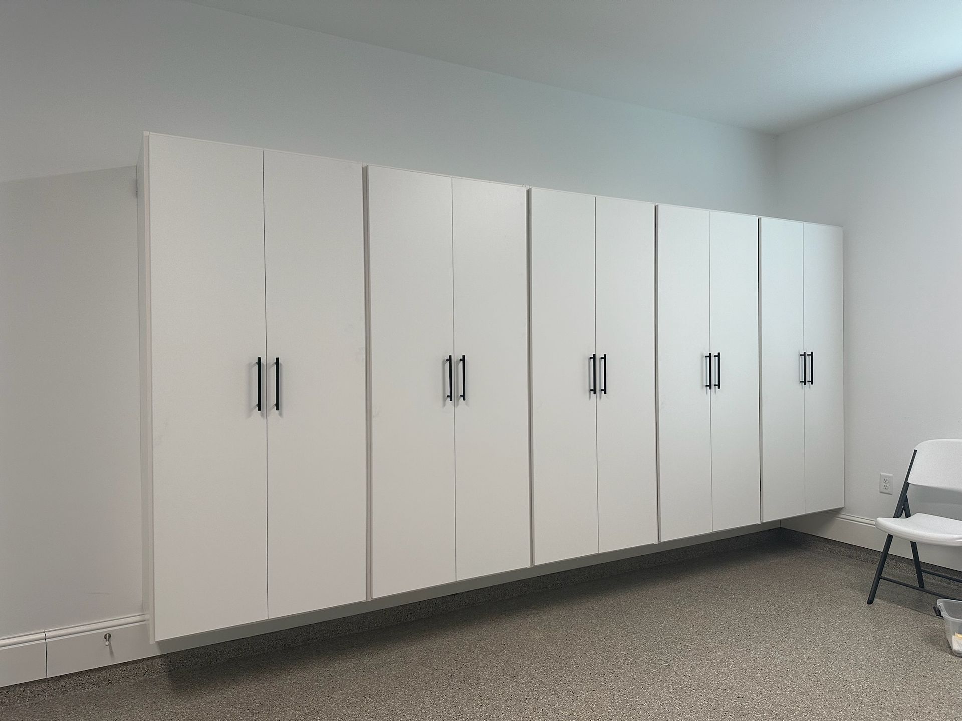 A row of white wall-mounted storage cabinets with modern handles, installed against a plain wall above a speckled floor.