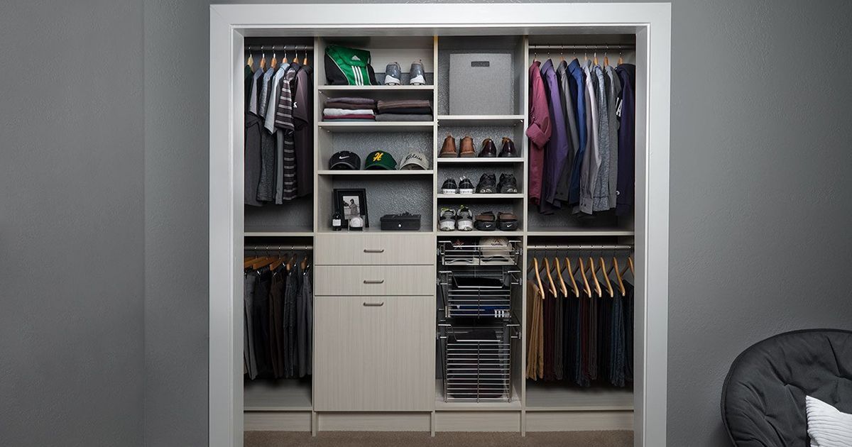 Walk-in closet with clothes hanging on rods, shelves, and drawers. Neutral color scheme with light gray and tan.