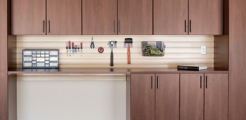 Garage workbench with gray cabinets, metal countertop, and tools hanging on a slatted wall.