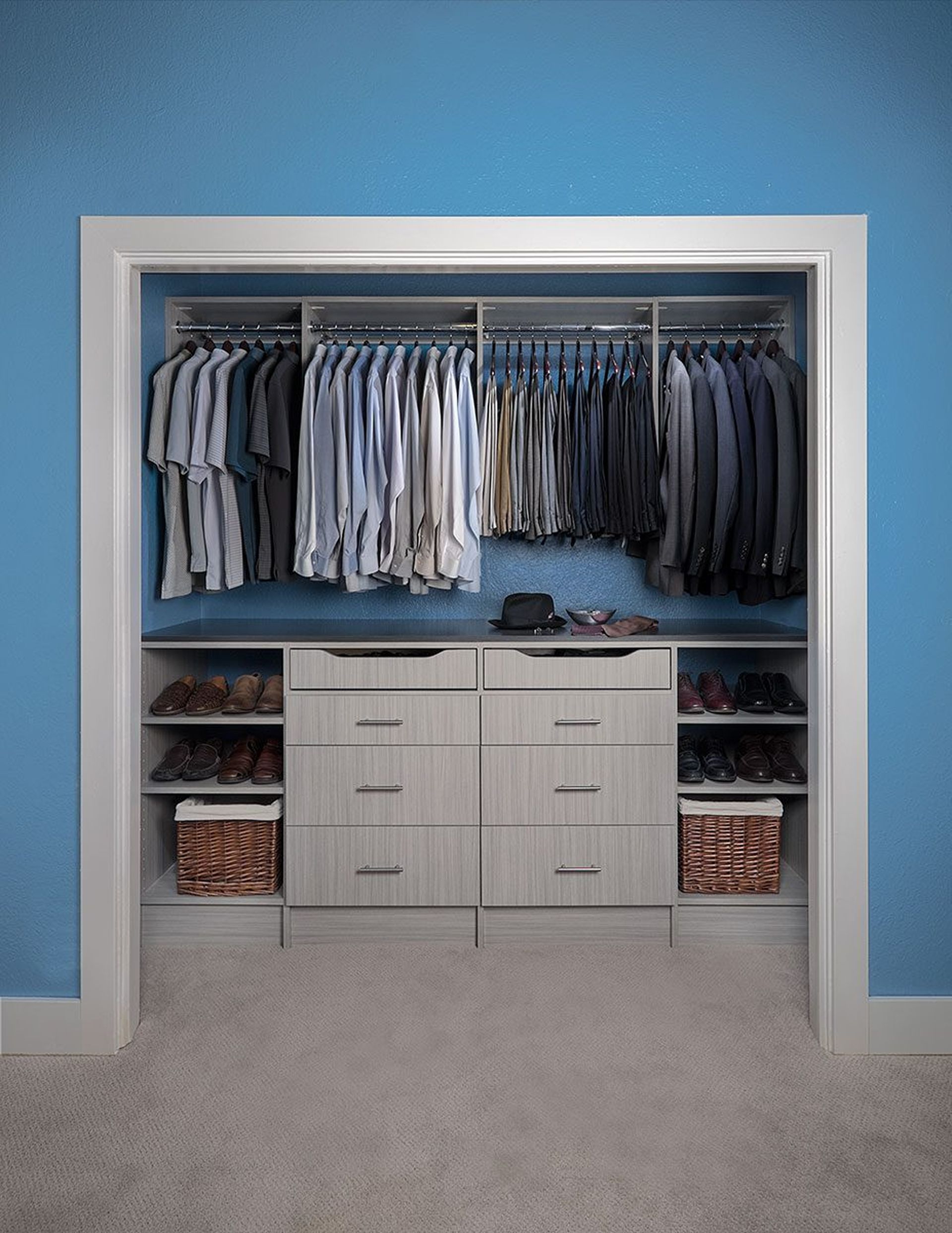 A reach in closet with gray shelving, drawers, and hanging rods for clothes. Clothing is organized by color.