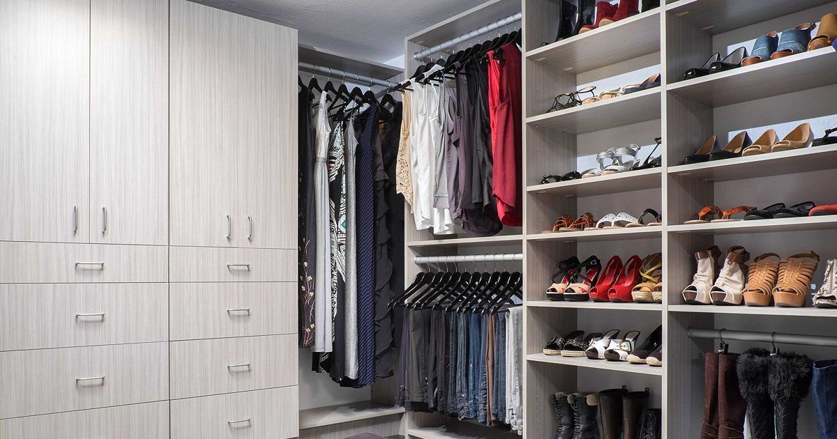 Walk-in closet with light-colored shelves, hanging clothes, shoes, and drawers.
