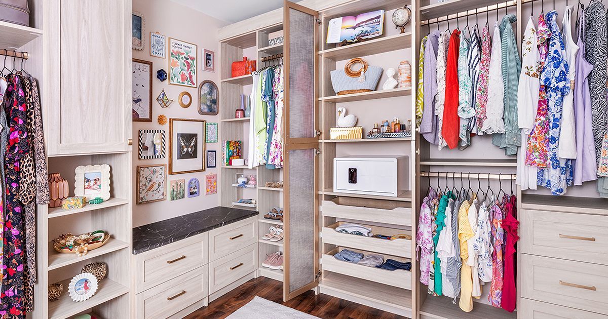 Walk-in closet with clothes, shelves, and drawers. Beige cabinets, clothing racks, and art adorn the walls.
