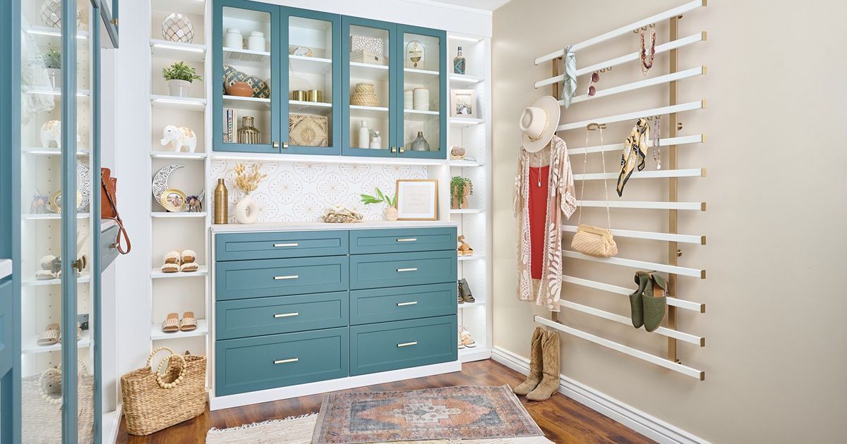 Walk-in closet with teal cabinetry, built-in shelves, a rug, and a white wall organizer with clothing and accessories.