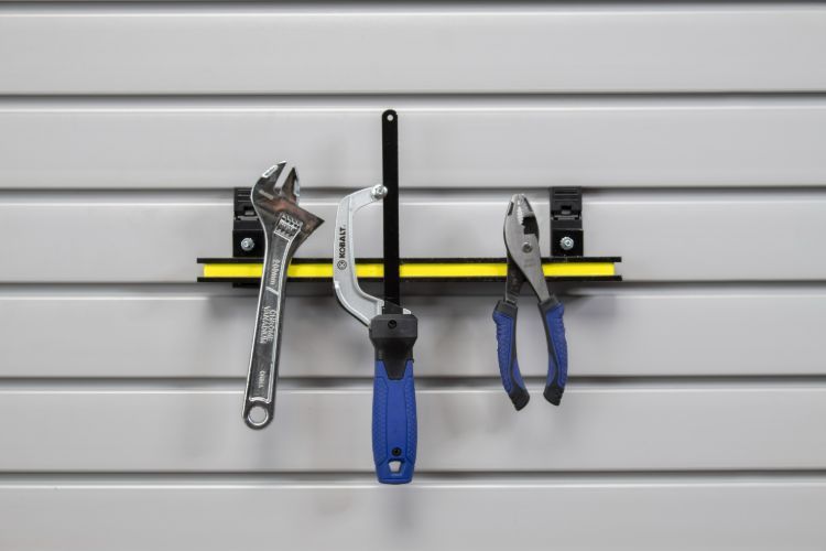 Tools (wrench, clamp, pliers) hanging on a horizontal track mounted on a wall with horizontal grooves.