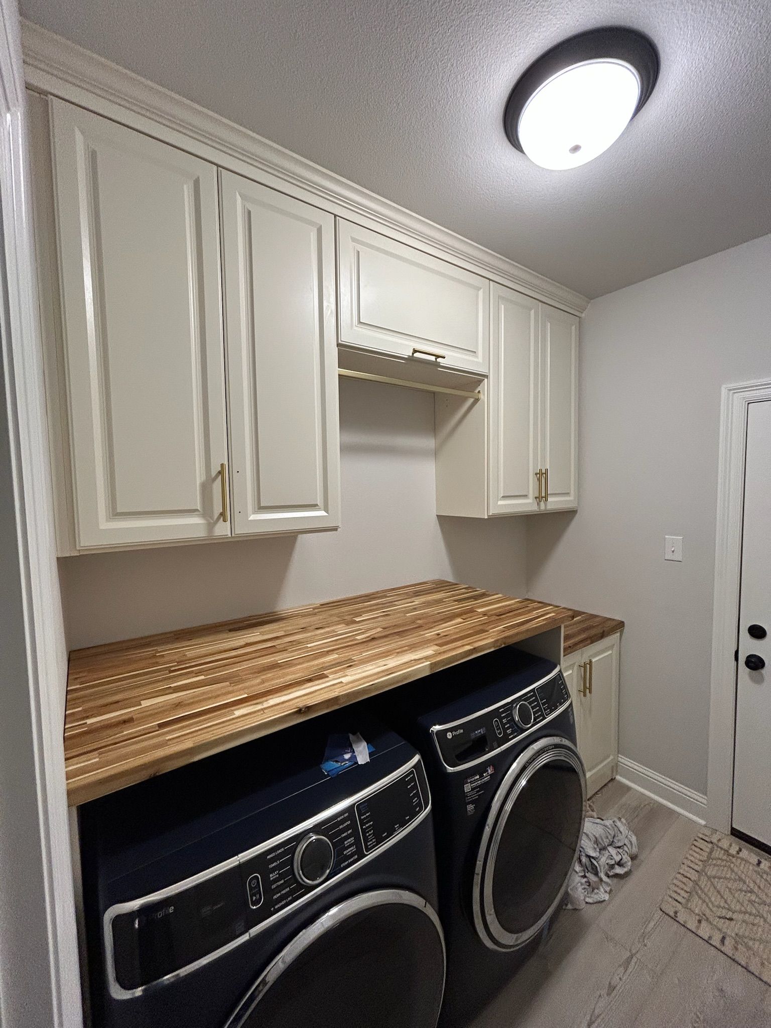 Laundry room with cream cabinets, wood countertop, blue washer and dryer, and overhead light.