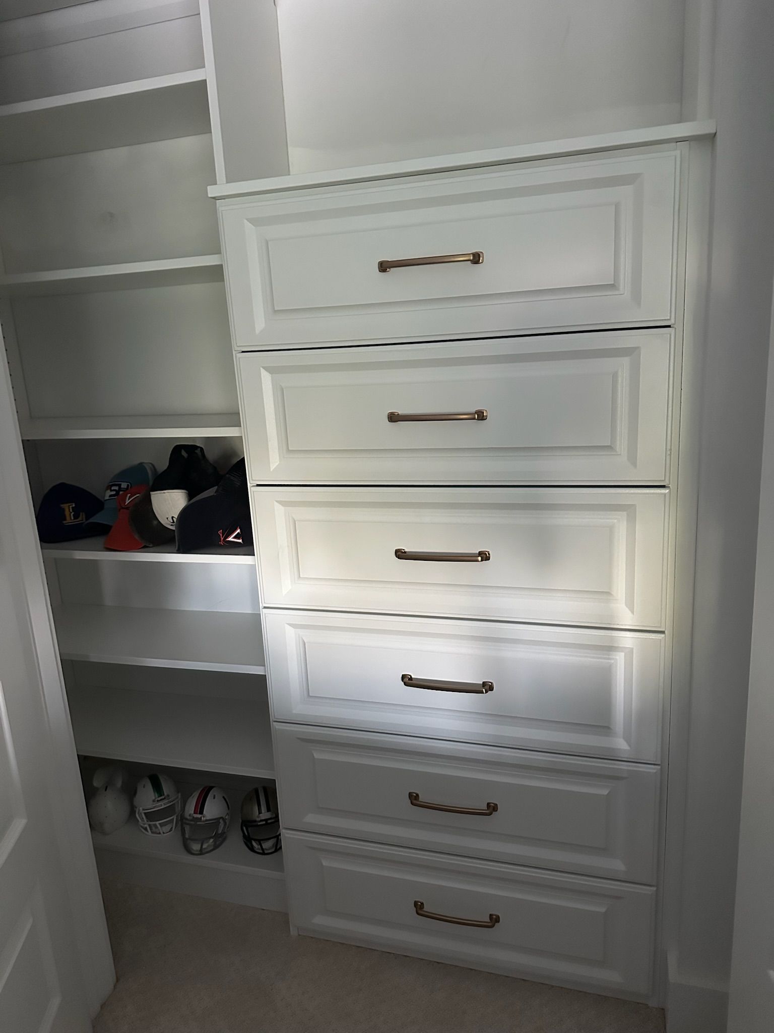 White closet with five drawers and bronze hardware; shoe and hat storage to the side.