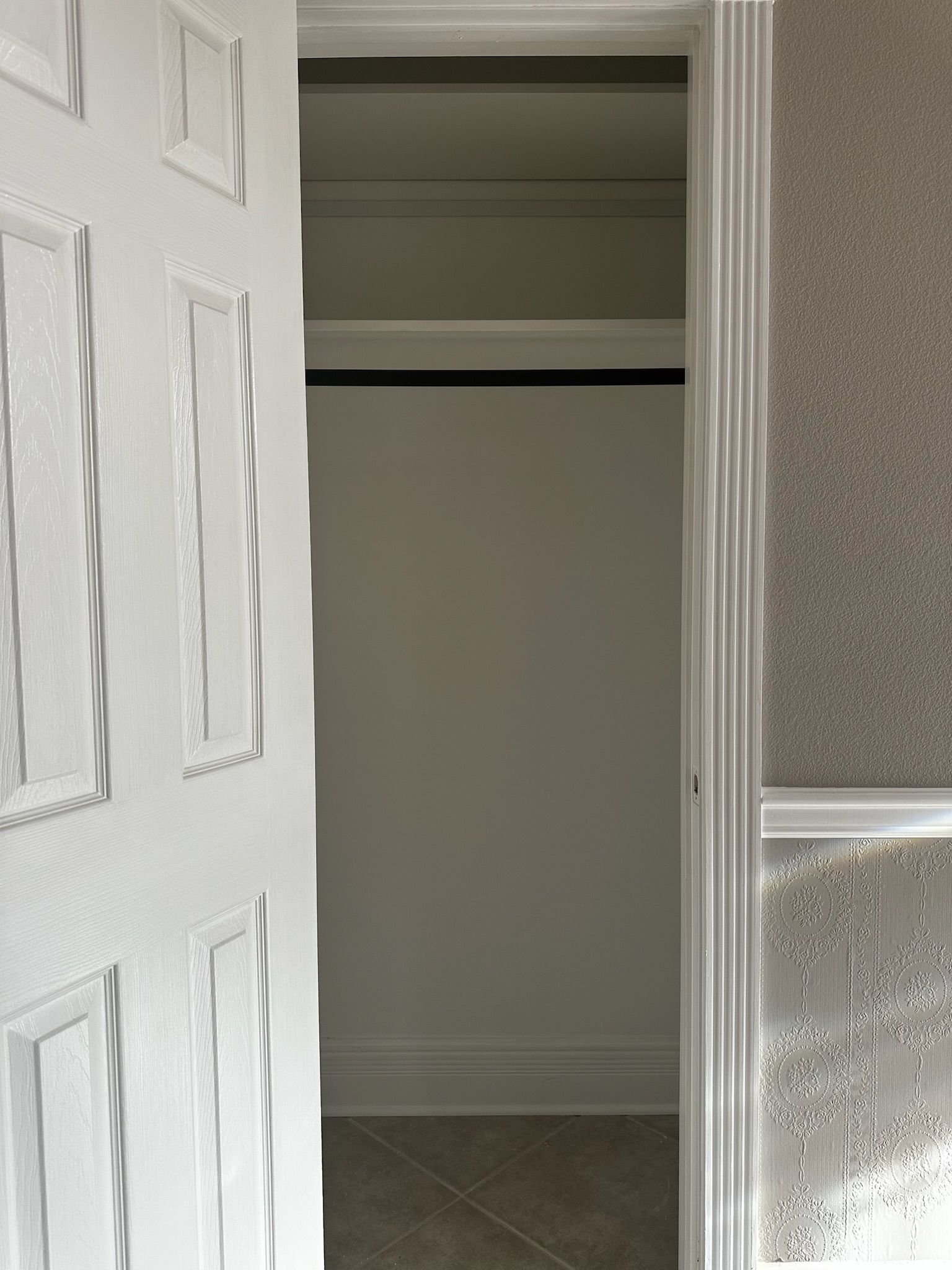 Open white door revealing an empty closet with a black rod. Light gray walls.