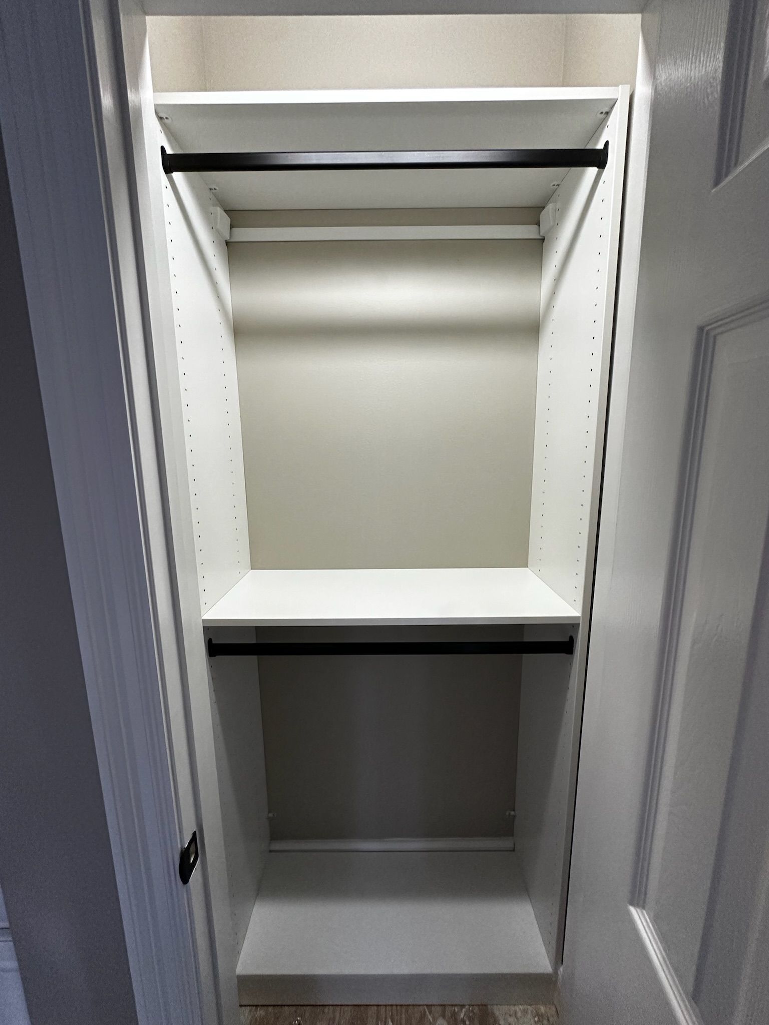 Empty white closet with two shelves and black rods.