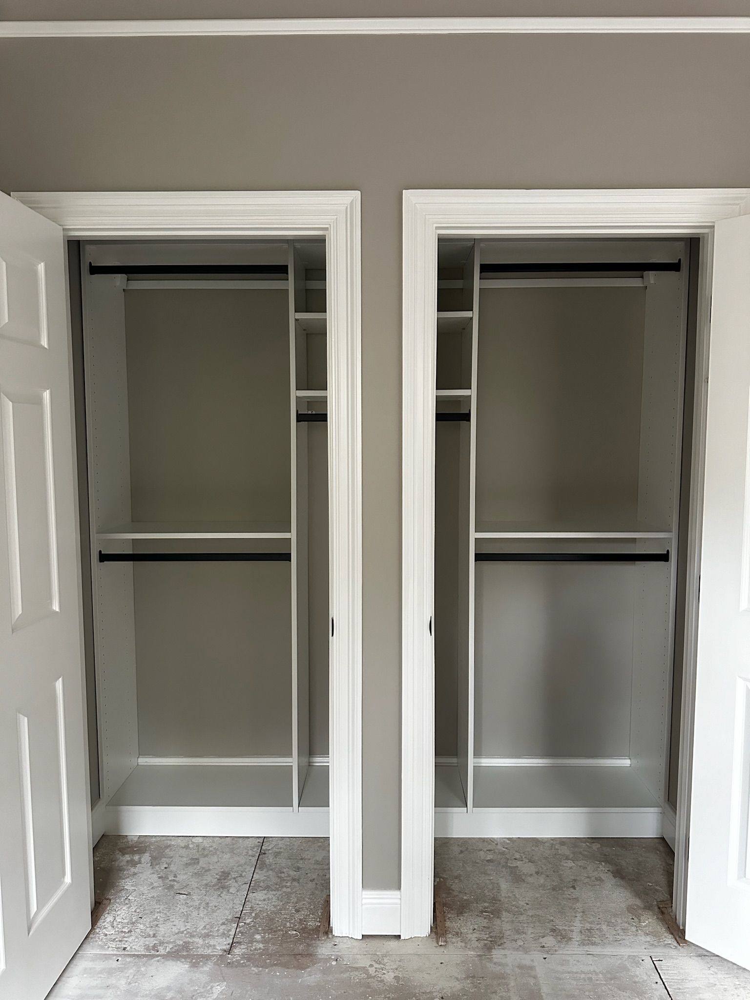 Two empty white closets side by side, with open doors, shelves, and hanging rods. Gray walls, and a light gray ceiling.