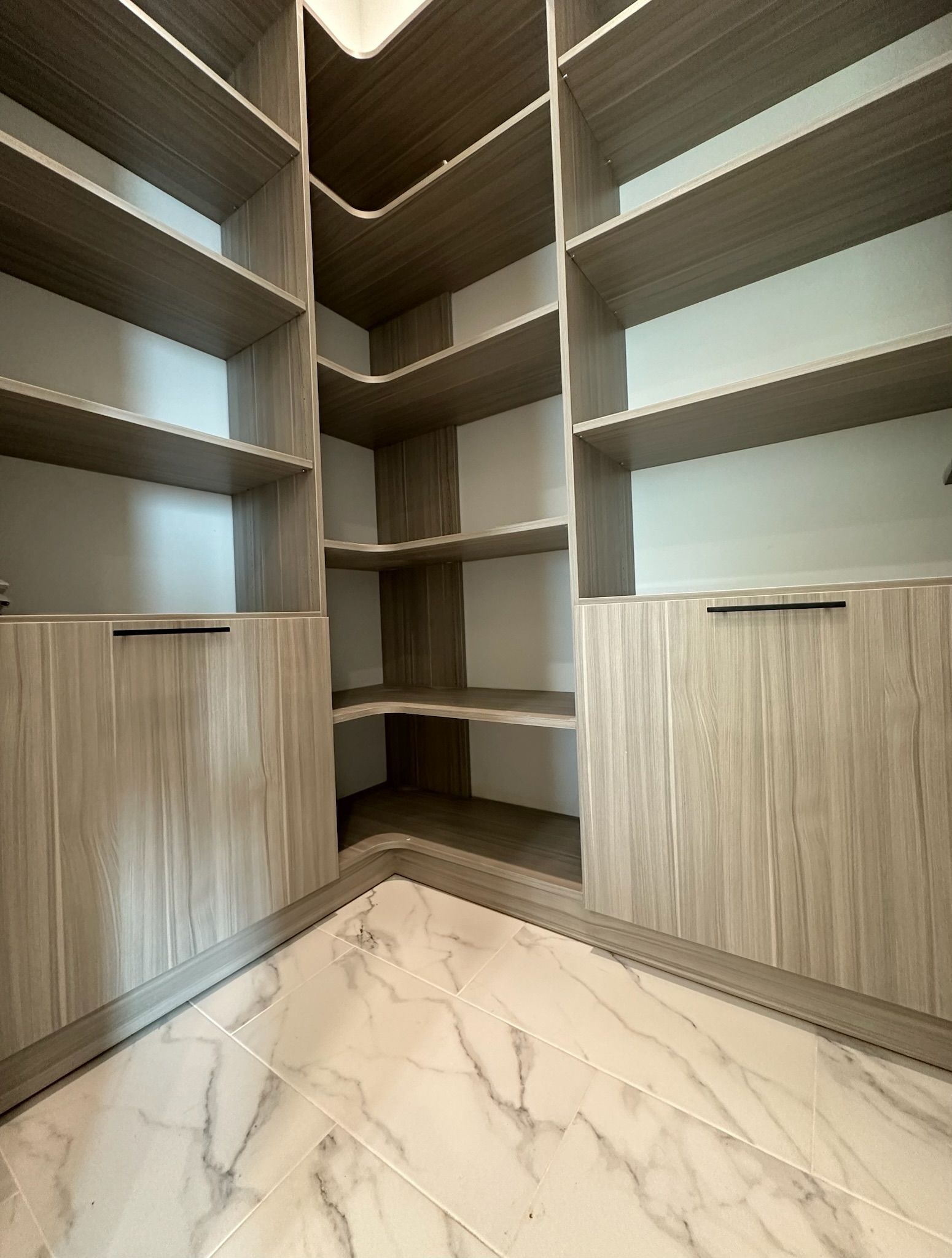 Walk-in closet with light wood shelves, drawers, and marble-look tile flooring. Corner shelves meet in the center.