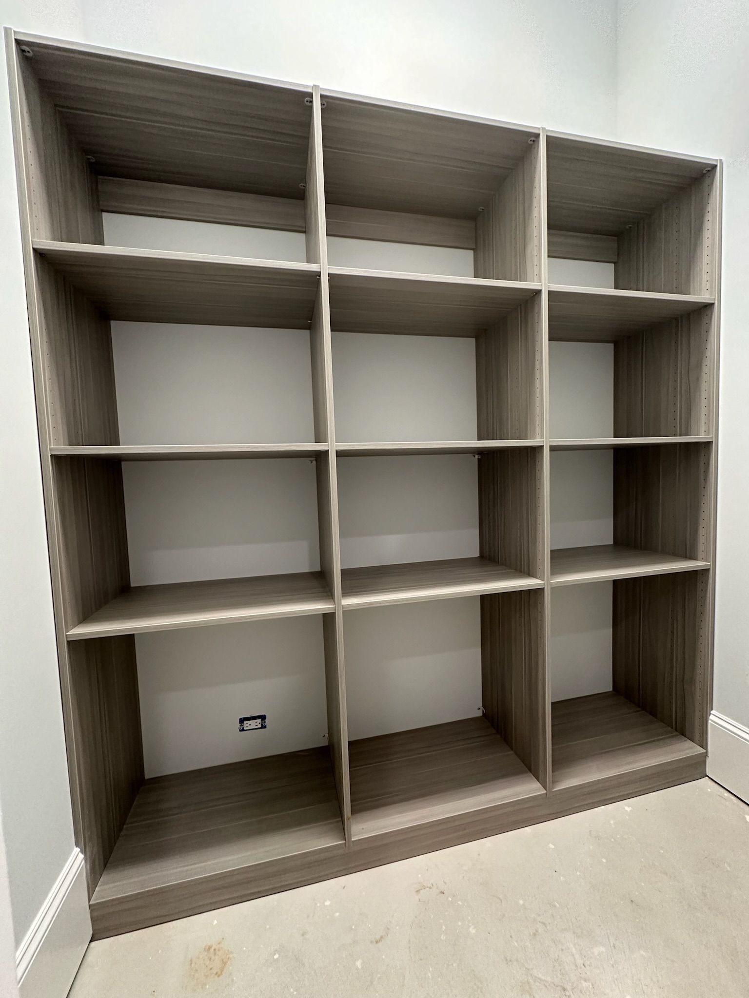 Empty wooden shelving unit with twelve compartments against a light wall.