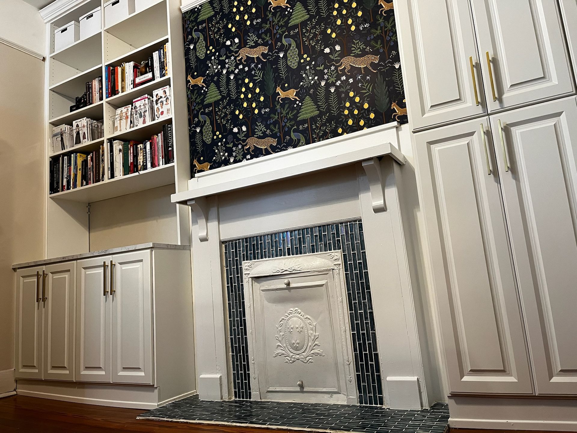 Built-in white cabinets and bookshelf surround a fireplace with decorative tile and forest-themed wallpaper.