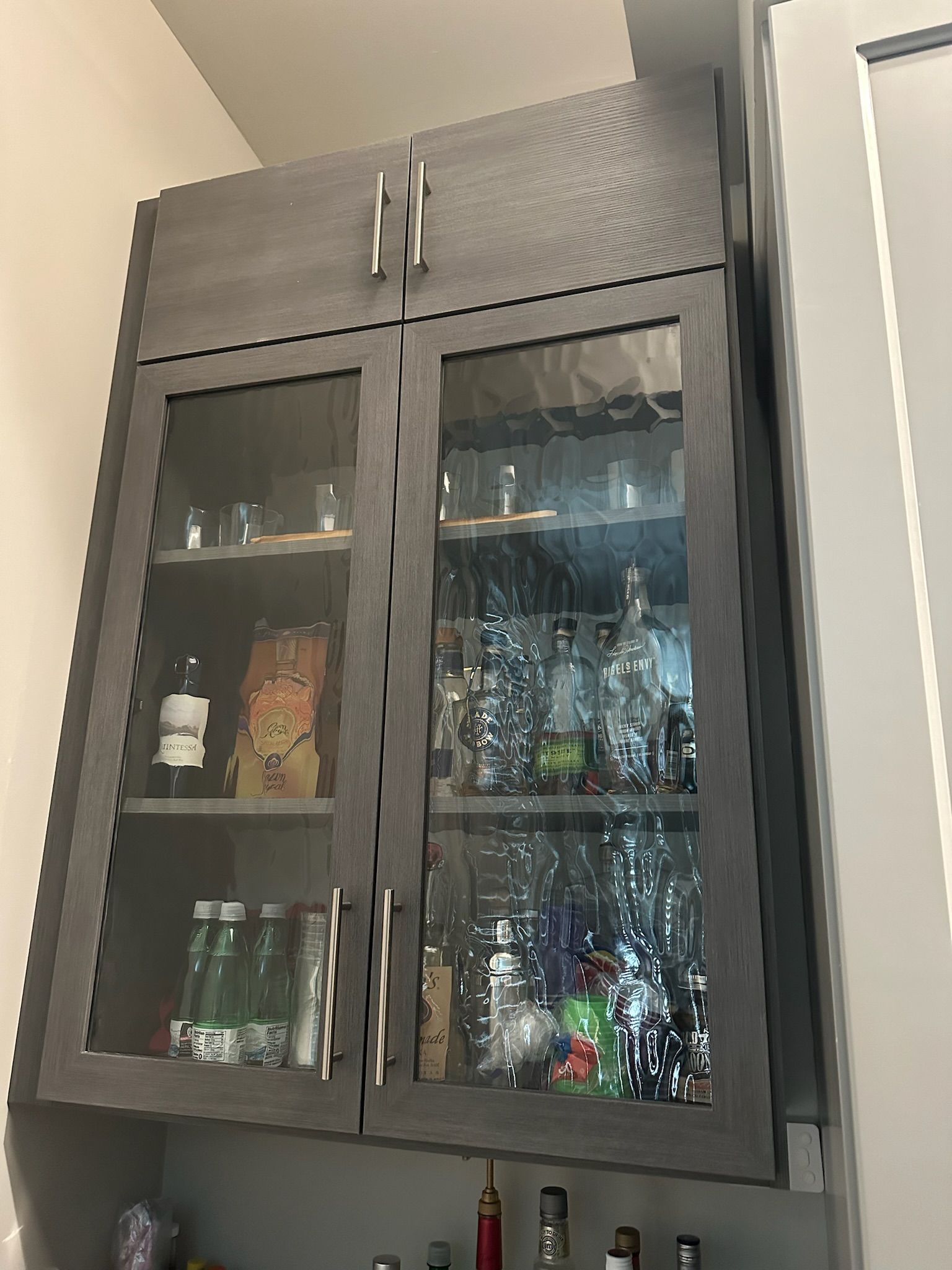 Gray cabinet with glass doors, stocked with bottles and glasses.