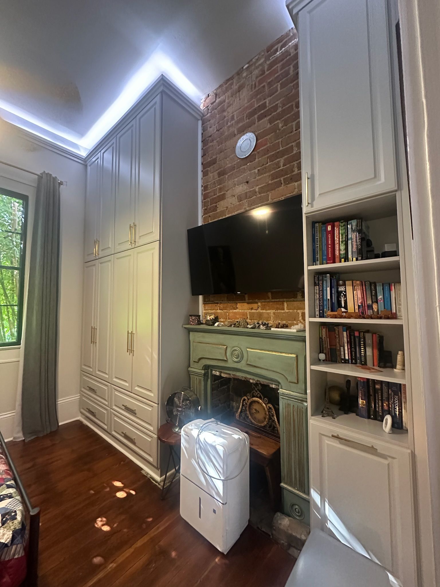 Bedroom with a large built-in wardrobe and bookshelf, a TV above a fireplace, and a dehumidifier.