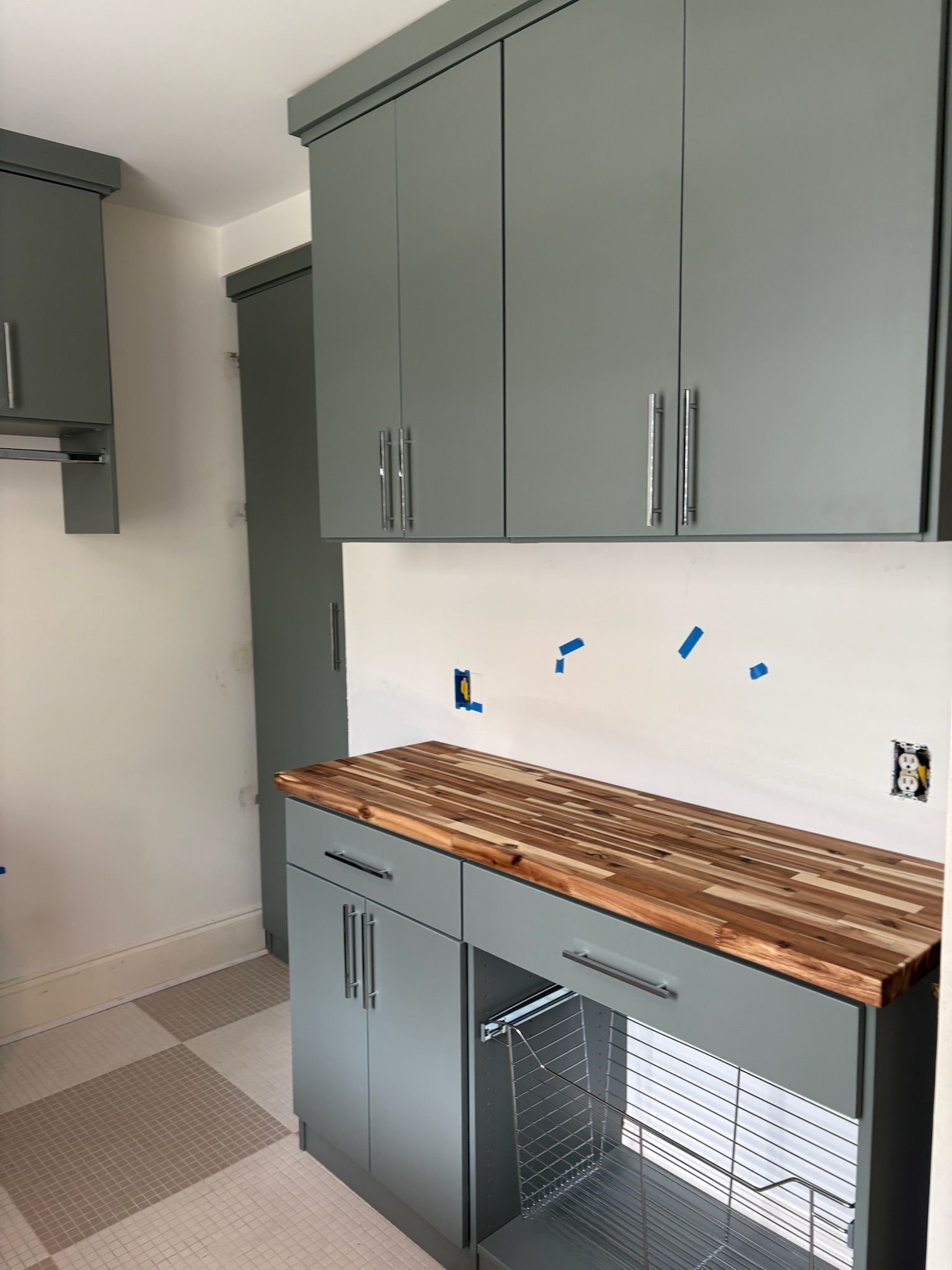 Grey kitchen cabinets with a butcher block countertop.