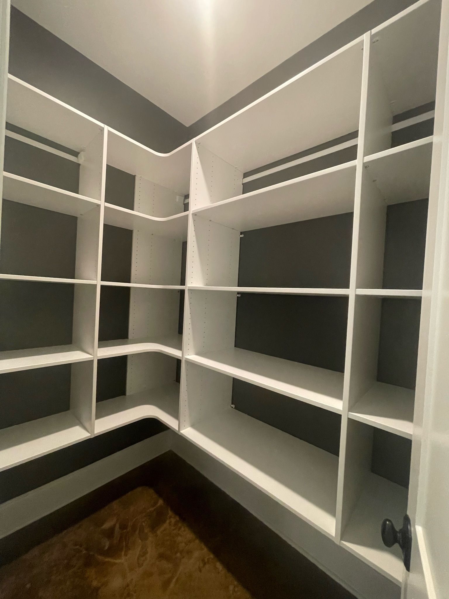 White pantry shelves against a gray wall. Corner shelves with brown floor.