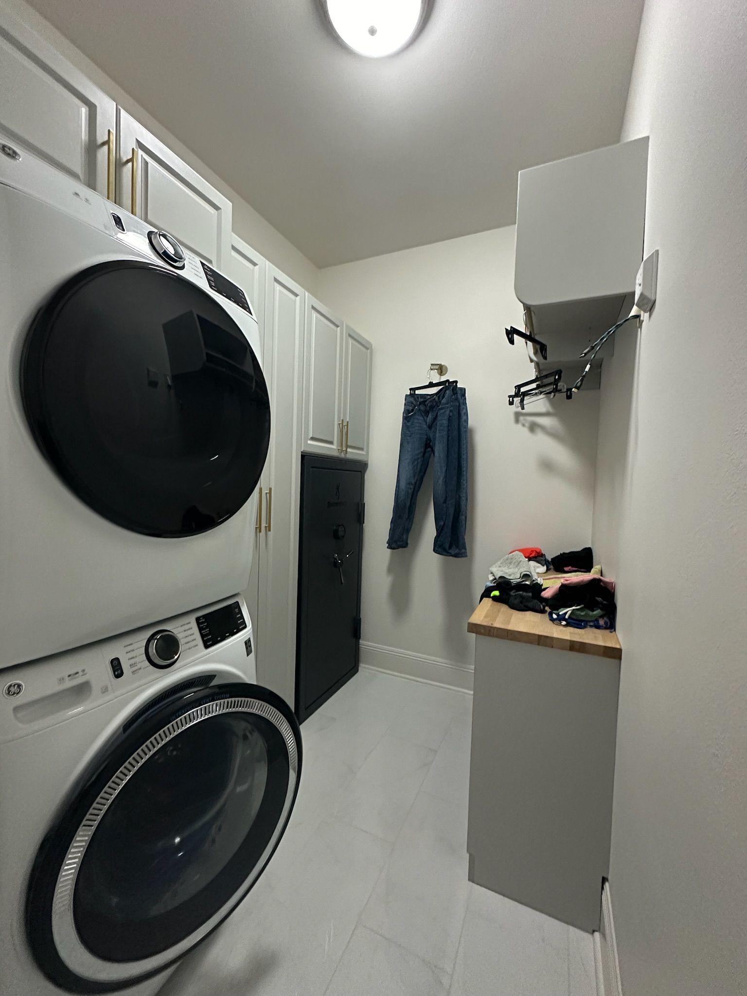 Laundry room with stacked white washer and dryer, cabinets, and hanging clothes.