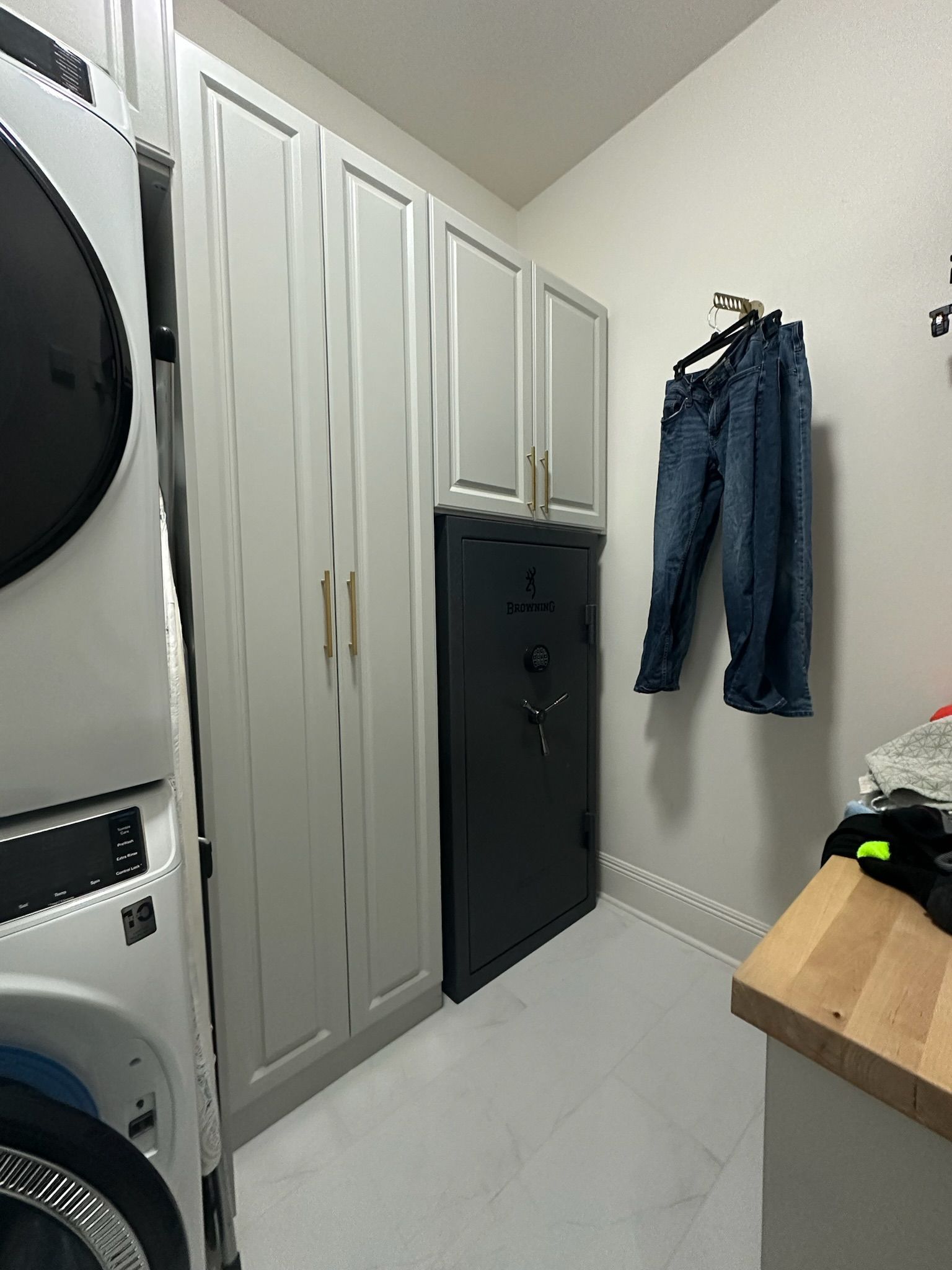 Laundry room with gray cabinets, a safe, washer/dryer, and blue jeans hanging.